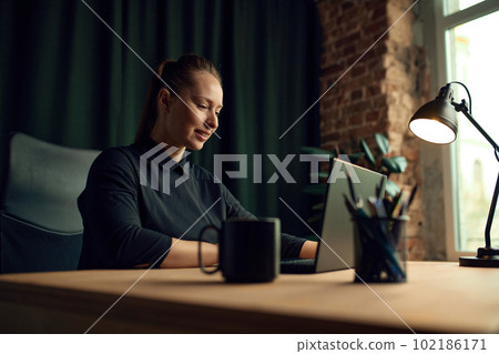 Smiling, happy, positive businesswoman sitting at table in her office, working on laptop with projects. Success 102186171