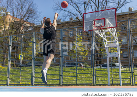 Athletic man in sportswear playing basketball game, successfully throws ball into the basket ring 102186782