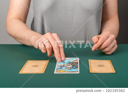 Lodz, Poland April 07 2023 Fortune teller spreading three tarot cards on green desk, reading, telling past, present and future. Cartomancy, divination concept 102195362