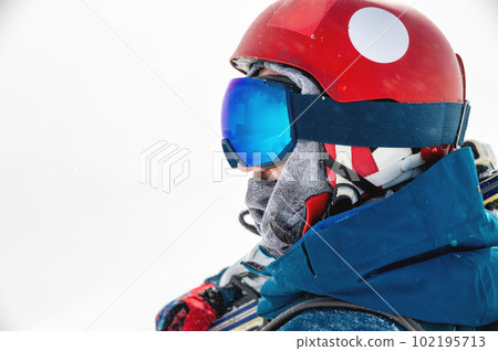 sportsman in a helmet and goggles in profile against the background of white falling snow, looks to the side enjoying a beautiful view of the mountains 102195713