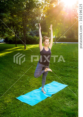 Young woman doing yoga exercises in the summer city park. 102196125