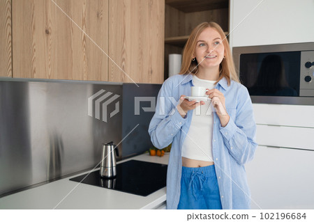 Young happy blonde woman drinking coffee on the kitchen in the morning Young happy blonde woman drinking coffee on the kitchen in the morning 102196684