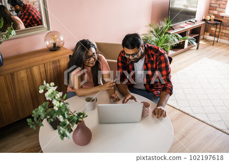 Latino or indian man and woman couple use their laptop in the living room to make video calls. Video call and online chat with family 102197618