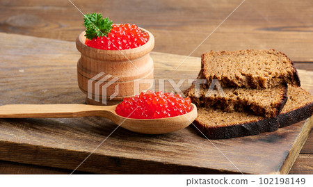 Red caviar in a wooden spoon, slices of bread on the table 102198149