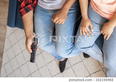 Close up couple sitting on sofa and watching action movie on TV or criminal blockbuster on streaming service and talking and discussing acting. Girlfriend and boyfriend resting at home in evening 102198468