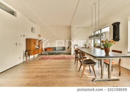 a living room with wood flooring and white walls, including a large dining table surrounded by two brown chairs a living room with wood flooring and white walls, including a large dining table surrounded by two brown chairs 102198689
