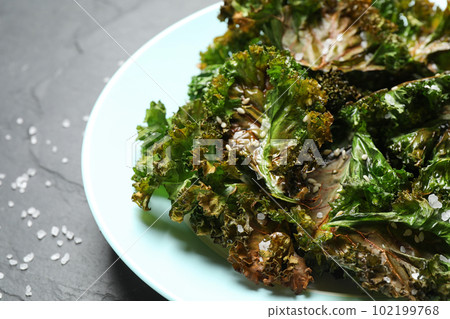 Tasty baked kale chips on dark grey table, closeup 102199768