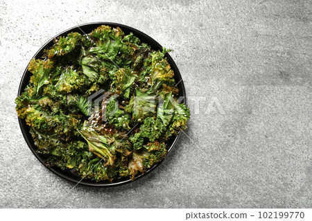 Tasty baked kale chips on grey table, top view 102199770