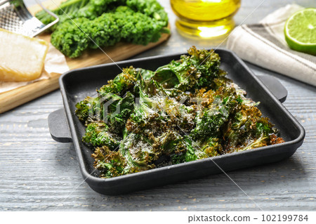 Tasty baked kale chips on grey wooden table 102199784