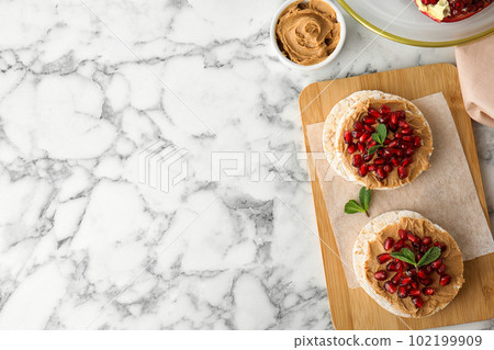 Puffed rice cakes with peanut butter and pomegranate seeds on white marble table, flat lay. Space for text Puffed rice cakes with peanut butter and pomegranate seeds on white marble table, flat lay. Space for text 102199909