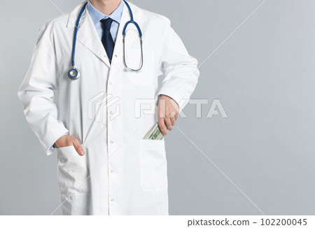 Doctor putting bribe money into pocket on grey background, closeup. Corruption in medicine 102200045