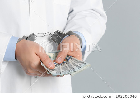 Doctor in handcuffs with bribe on grey background, closeup. Corrupted medicine Doctor in handcuffs with bribe on grey background, closeup. Corrupted medicine 102200046