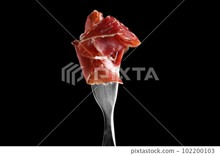 Tasty prosciutto on fork against black background 102200103