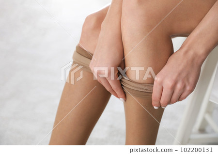 Beautiful woman putting on tights indoors, closeup Beautiful woman putting on tights indoors, closeup 102200131