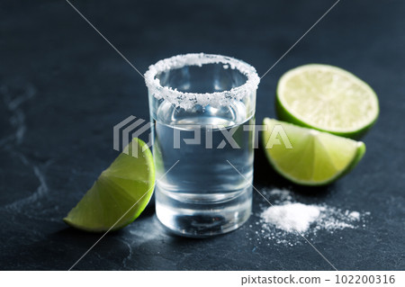 Mexican Tequila shot, lime slices and salt on grey table Mexican Tequila shot, lime slices and salt on grey table 102200316