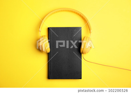 Book and modern headphones on yellow background, top view 102200326