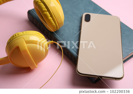 Book, modern headphones and smartphone on pink background, closeup Book, modern headphones and smartphone on pink background, closeup 102200336