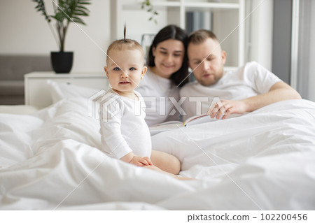 Mother and father reading verse book for baby daughter 102200456
