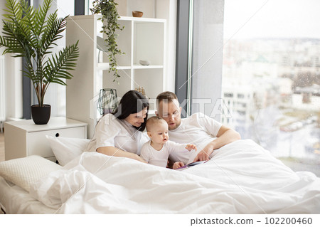 Parents looking through picture book with daughter in bed 102200460