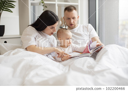 Parents looking through picture book with daughter in bed 102200466