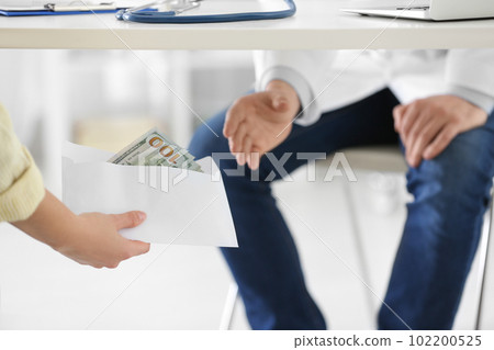 Patient giving bribe to doctor under table in clinic, closeup. Corrupted medicine 102200525