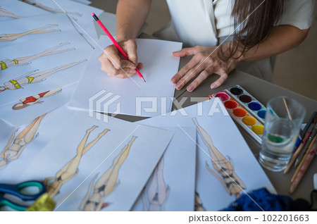 Faceless woman draws sketches of swimwear with a pencil. Close-up of the hands of a fashion designer. 102201663