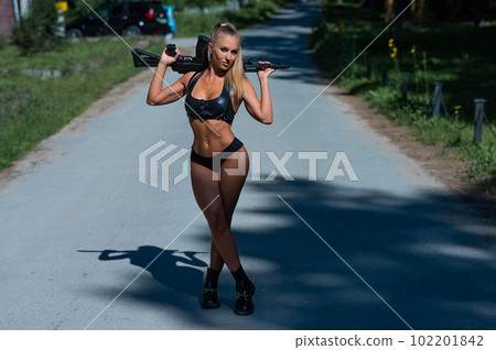 Caucasian woman in bikini with machine gun outdoors. 102201842