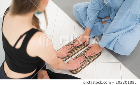 Two women sit on yoga mats with their hands on sadhu boards.  102201883