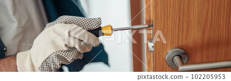 Close up of locksmith workman in uniform installing door knob. Professional repair service Close up of locksmith workman in uniform installing door knob. Professional repair service 102205953