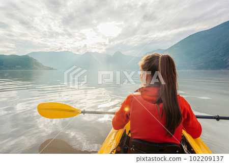 Woman kayaking paddling in kayak in fjord surrounded by mountains. People living healthy active outdoor lifestyle. From Howe Sound, Squamish, British Columbia, Canada Woman kayaking paddling in kayak in fjord surrounded by mountains. People living healthy active outdoor lifestyle. From Howe Sound, Squamish, British Columbia, Canada 102209137
