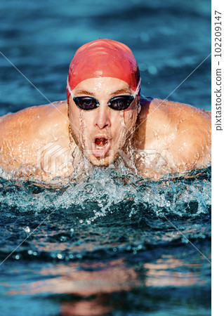 Man Swimming. Male Swimmer athlete doing butterfly swim stroke. Male sport fitness man wearing swimming goggles and swim cap training hard in outdoor pool. Professional sports fitness model Man Swimming. Male Swimmer athlete doing butterfly swim stroke. Male sport fitness man wearing swimming goggles and swim cap training hard in outdoor pool. Professional sports fitness model 102209147