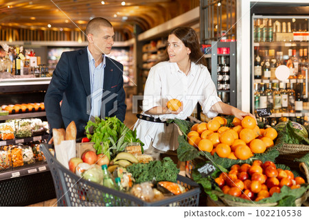 Happy young couple with a grocery cart in the supermarket shooses tangerines Happy young couple with a grocery cart in the supermarket shooses tangerines 102210538