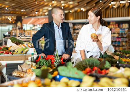 Positive young couple with a grocery cart in the supermarket, choose pears Positive young couple with a grocery cart in the supermarket, choose pears 102210661