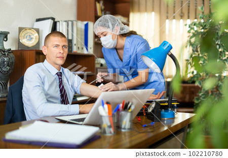 Nurse giving vaccine injection to man in office 102210780