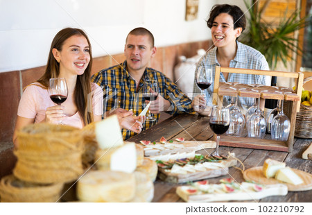 Company of friends tasting cheese and drinking wine while spending time together in winery, indoors 102210792