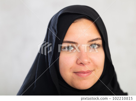 young calm Muslim woman in traditional hijab clothes poses on gray background. 102210815