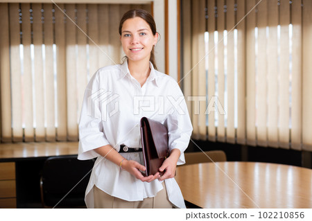 Portrait of a young girl standing in a conference room, holding a folder of documents 102210856
