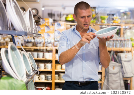 Attentive man choosing new crockery in dinnerware store closeup Attentive man choosing new crockery in dinnerware store closeup 102210872