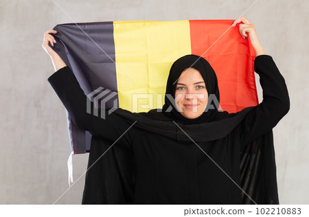 Balanced Muslim woman in traditional black hijab holds flag of Belgium Balanced Muslim woman in traditional black hijab holds flag of Belgium 102210883