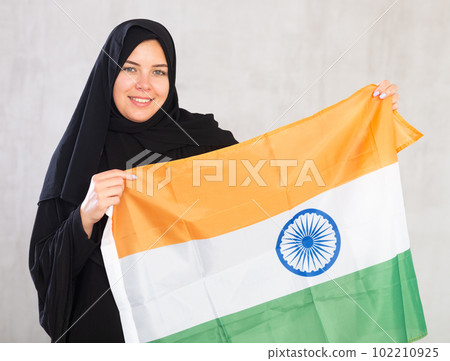 Balanced smiling Muslim woman in traditional black hijab holds flag of India 102210925