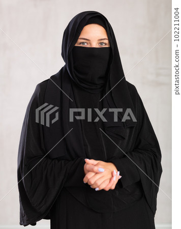 Muslim woman with face covered with burka holds thin fabric of yashmak with her hands Muslim woman with face covered with burka holds thin fabric of yashmak with her hands 102211004