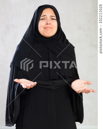 young Muslim woman in black hijab is upset by bad news and dejectedly holds her hands palms up. 102211026