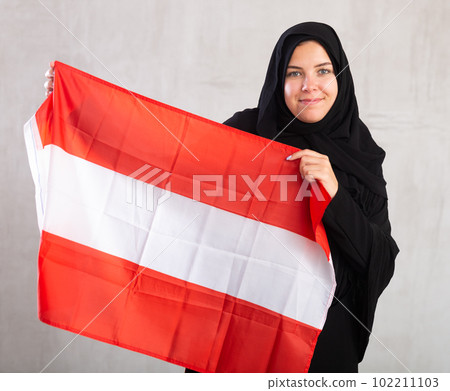 smiling Muslim woman in traditional black hijab holds flag of Austria smiling Muslim woman in traditional black hijab holds flag of Austria 102211103