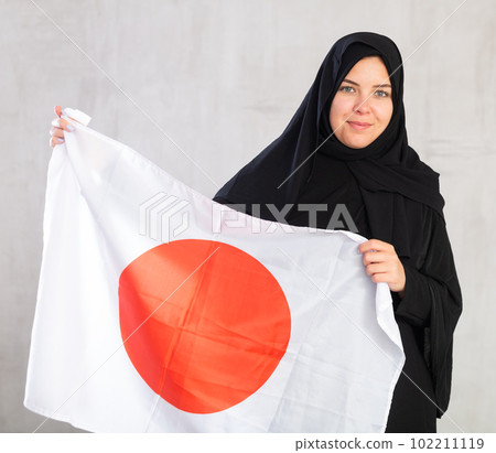 Balanced Muslim woman in traditional black hijab holds flag of Japan Balanced Muslim woman in traditional black hijab holds flag of Japan 102211119