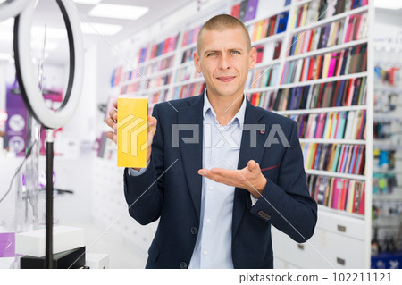Smiling male holding box with a mobile phone in the hand at electronics store Smiling male holding box with a mobile phone in the hand at electronics store 102211121