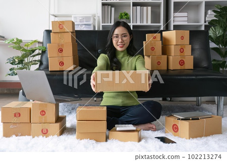 Young business woman working online e-commerce shopping at home. Young woman seller prepare parcel box of product for deliver to customer. Online selling Young business woman working online e-commerce shopping at home. Young woman seller prepare parcel box of product for deliver to customer. Online selling 102213274