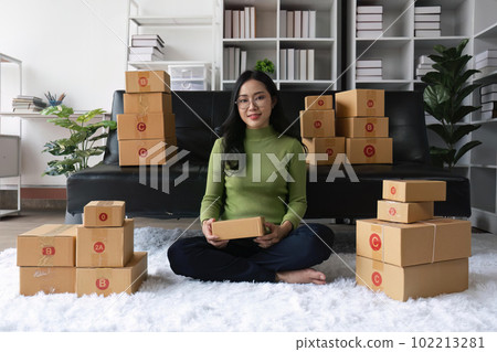 Young business woman working online e-commerce shopping at home. Young woman seller prepare parcel box of product for deliver to customer. Online selling 102213281
