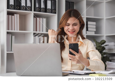 Success at work, good deal. Asian business woman looks at the laptop screen, screams excitedly and raises his fists in a victory gesture Success at work, good deal. Asian business woman looks at the laptop screen, screams excitedly and raises his fists in a victory gesture 102213509
