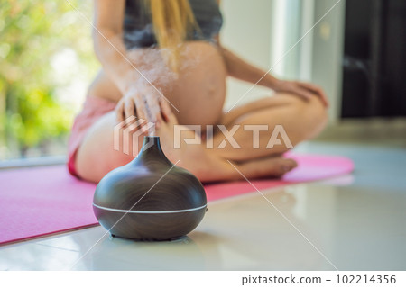 Young pregnant woman doing yoga exercises and meditating at home with an aroma diffuser. Health care, mindfulness, relaxation and wellness concept. Aromatherapy during pregnancy Young pregnant woman doing yoga exercises and meditating at home with an aroma diffuser. Health care, mindfulness, relaxation and wellness concept. Aromatherapy during pregnancy 102214356