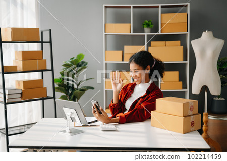Startup small business SME, Entrepreneur owner African woman using smartphone or tablet taking receive and checking online purchase shopping order to preparing pack product box. in office 102214459